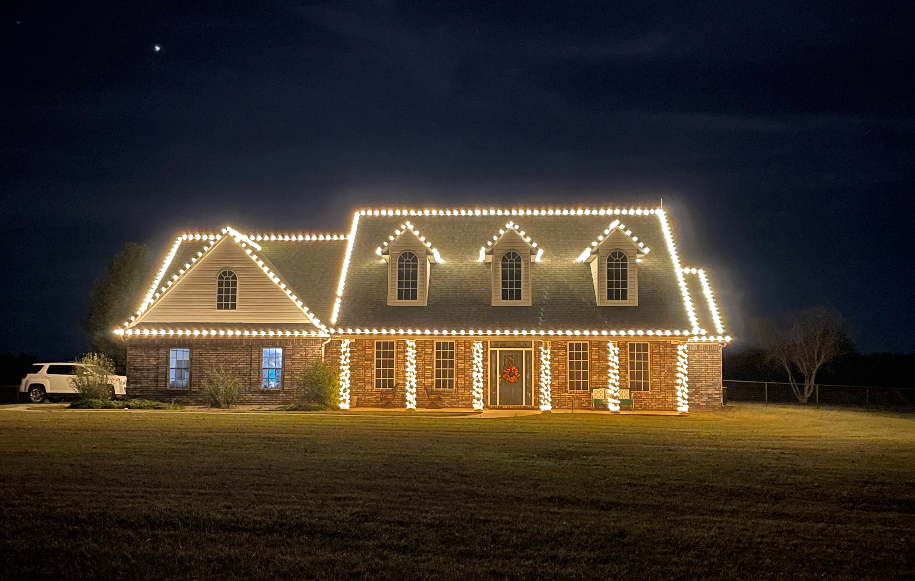 Cape cod home with warm white holiday lights outlining every dormer and roofline