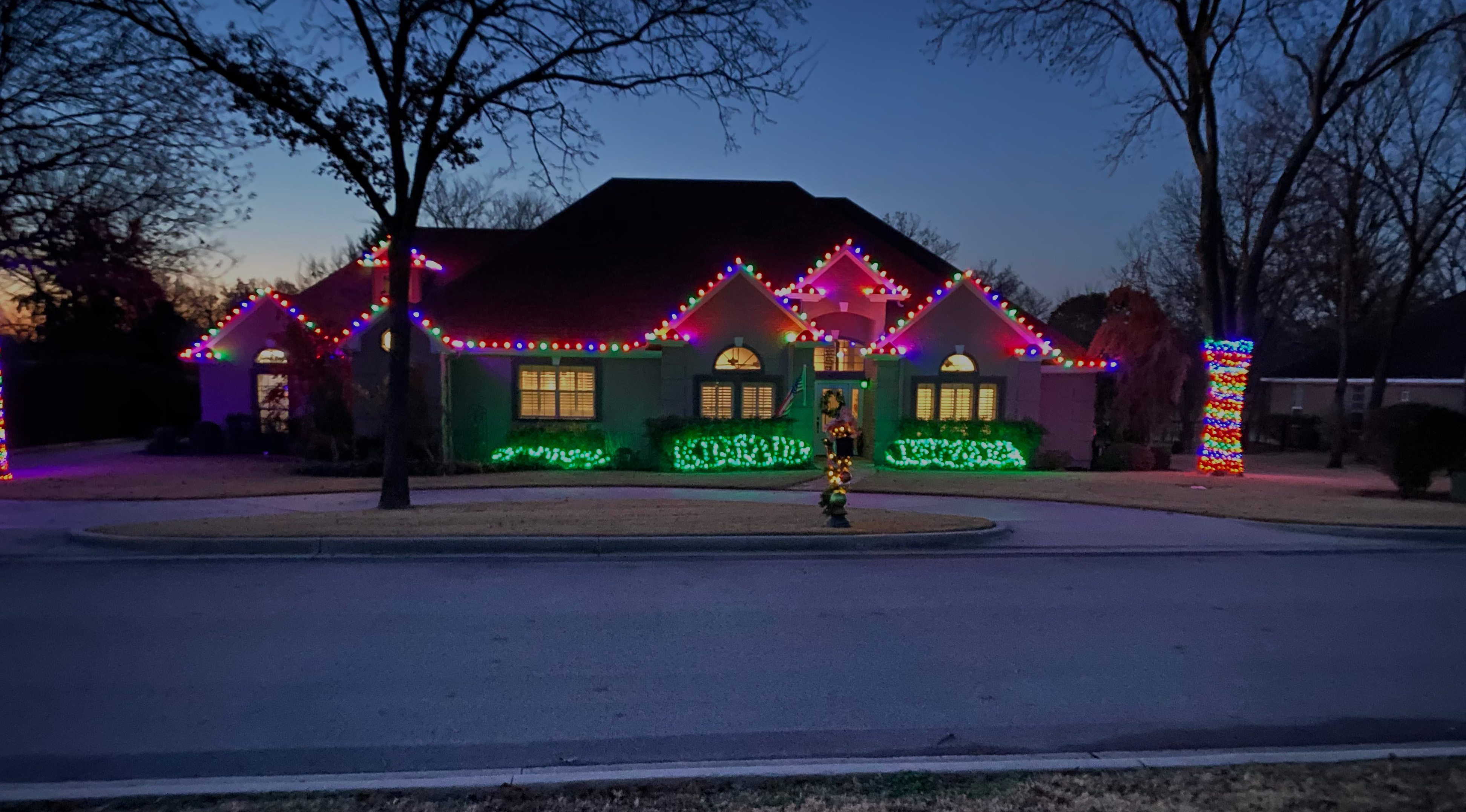 Corner home with multicolor roofline lights, lit corner columns, and yard displays