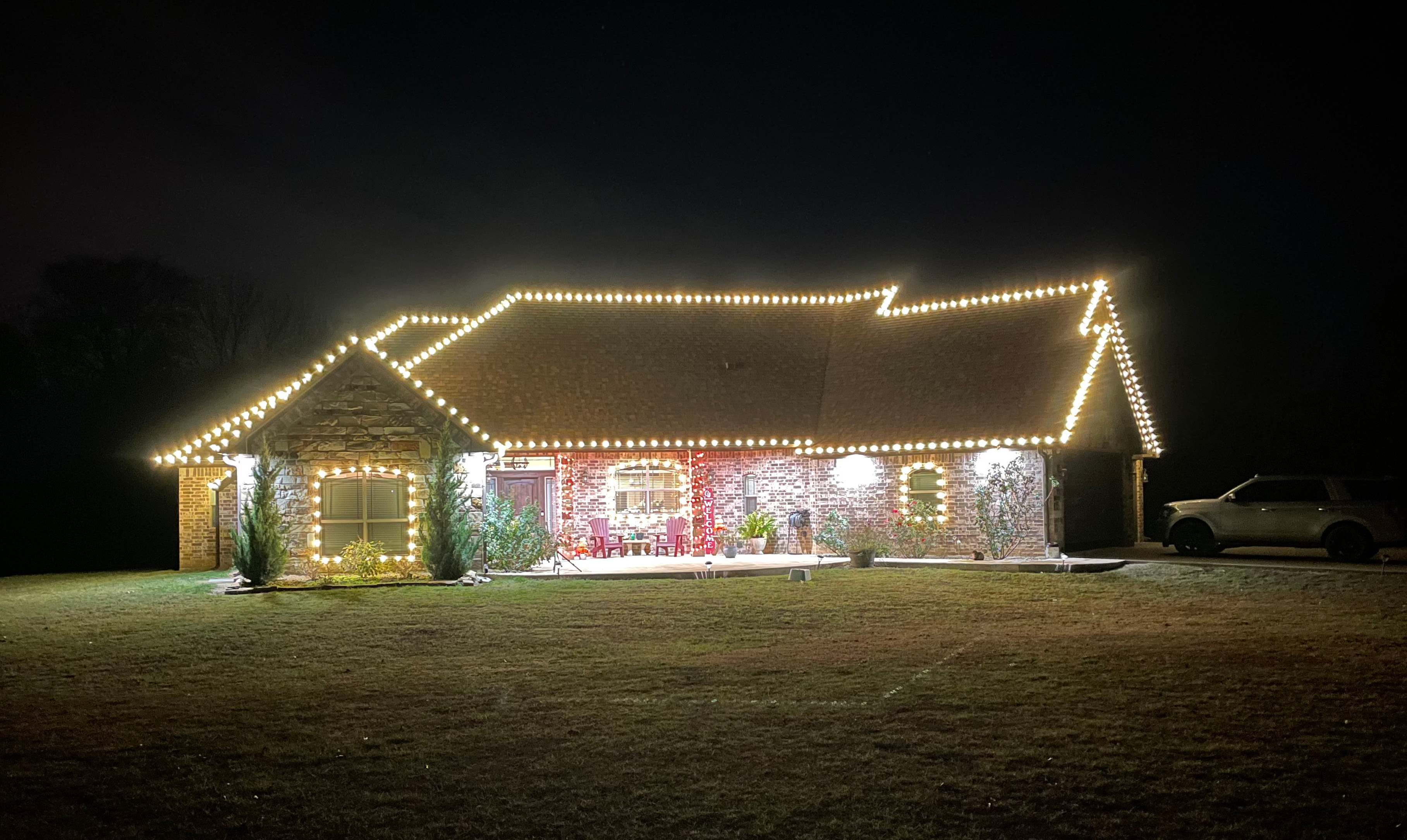 Farmhouse with warm white holiday lights outlining the roofline, dormers, and columns
