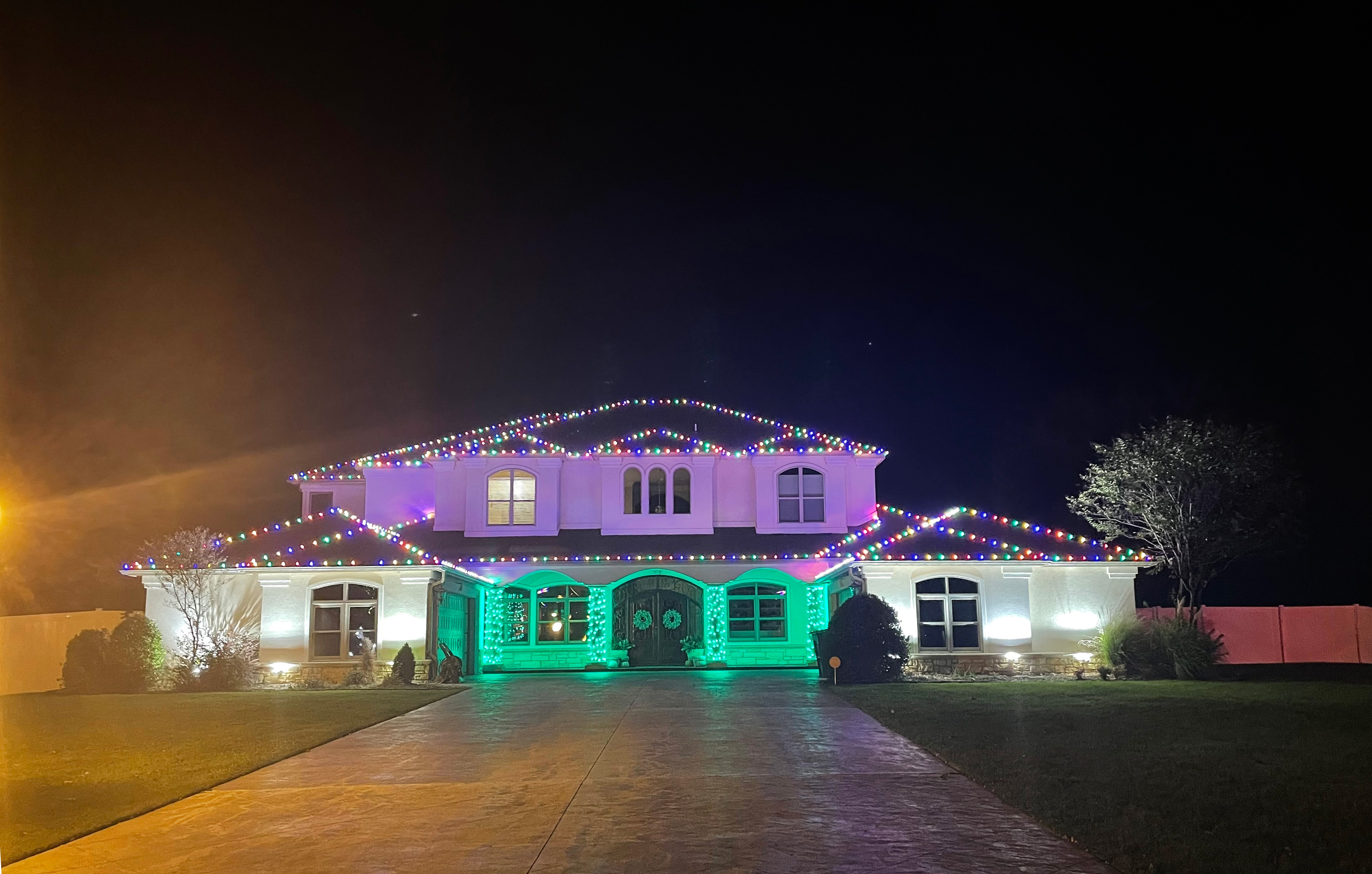 Mediterranean estate with multicolor roofline lights and green entry lighting