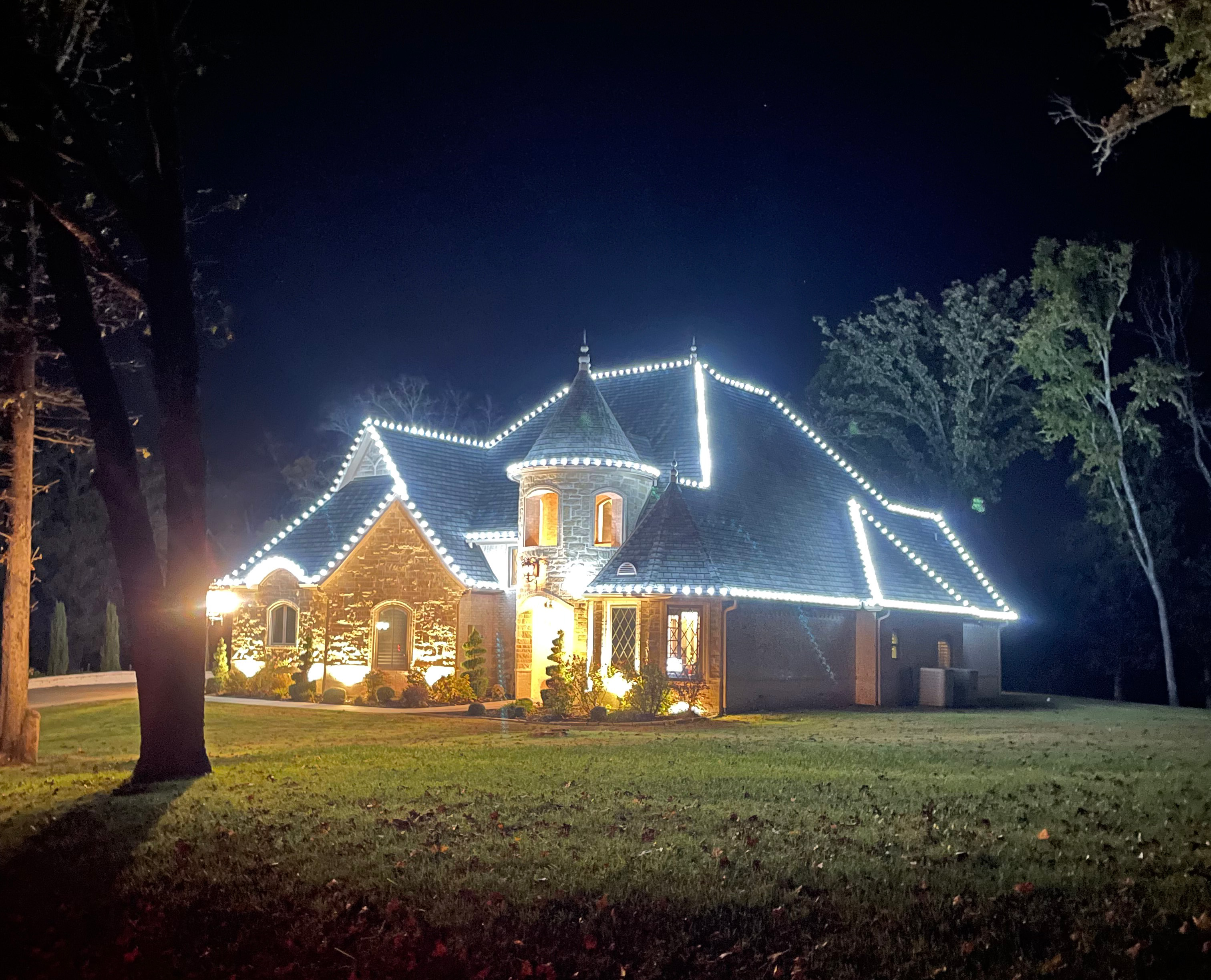 Stone turret home with white holiday lights tracing every roofline and gable
